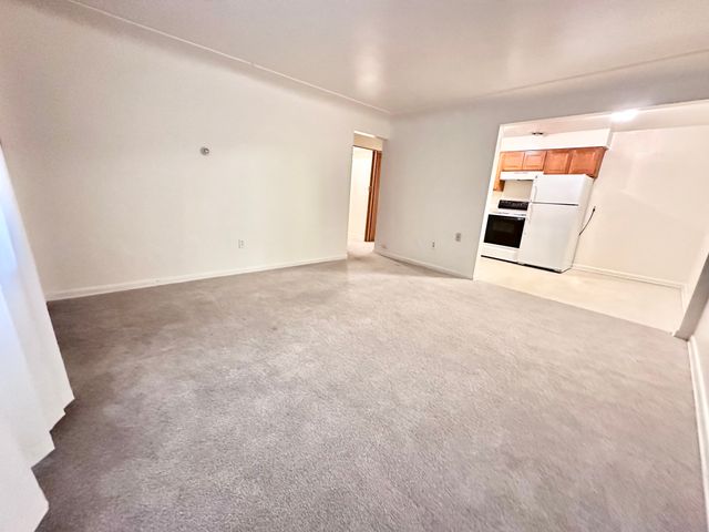 Bright and inviting living room with plush carpeting, seamlessly connecting to a cozy kitchen area.