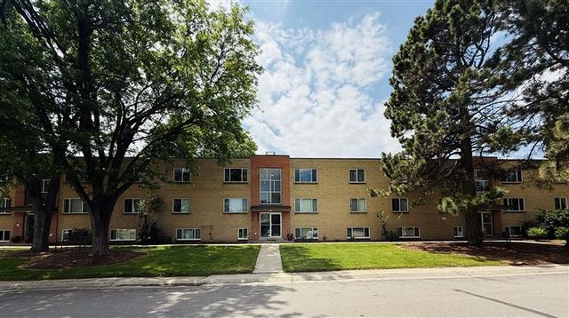 Charming apartment building surrounded by lush trees and well-maintained green lawn, offering a serene and inviting atmosphere.