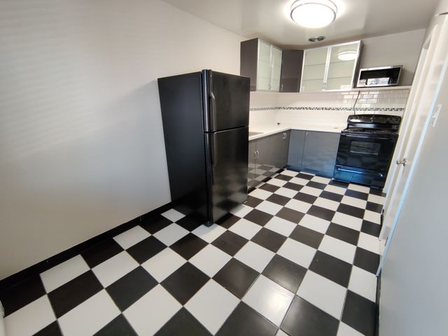 Modern kitchen with sleek black and white checkered flooring, stylish black appliances, and ample cabinet space.