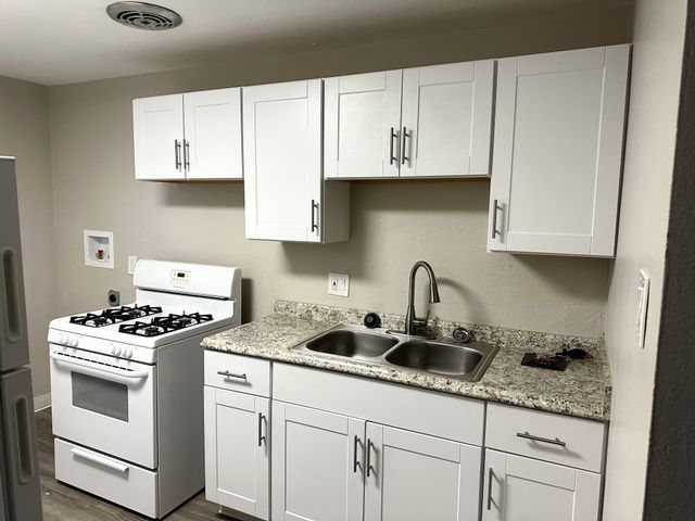 Modern kitchen with sleek white cabinets, granite countertops, and a four-burner stove offering a contemporary cooking space.