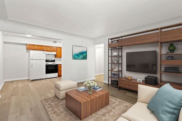 Inviting open-concept living room with contemporary furniture and a cozy rug, adjacent to a well-equipped kitchen with wooden cabinets and modern appliances.