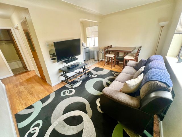 Inviting living room with modern TV setup, cozy sofa, and elegant dining area, enhanced by natural light and stylish decor.