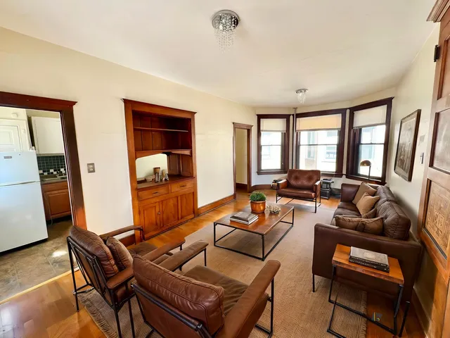 Inviting living room with elegant leather seating, warm wooden accents, and ample natural light from large windows.