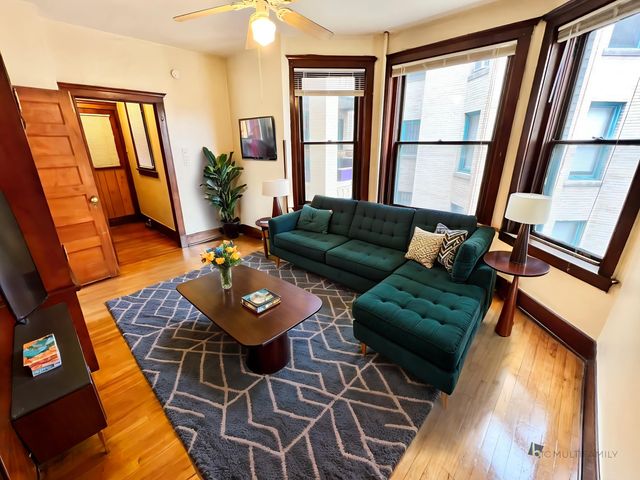 Bright and inviting living room with large windows, featuring a plush emerald green couch, stylish wooden coffee table, and modern decor.