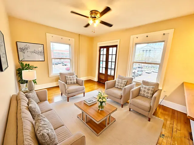 Bright and inviting living room with cozy beige seating, hardwood floors, and large windows offering city views.