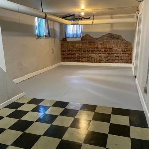 Charming basement space featuring exposed brick walls, industrial pipes, and checkerboard flooring, offering a cozy and rustic charm.