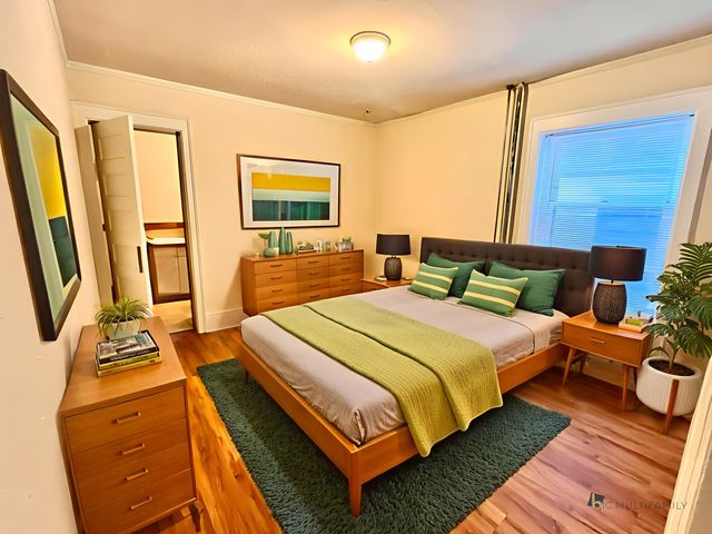 Inviting bedroom with modern decor, featuring hardwood floors, vibrant green accents, and ample natural light.