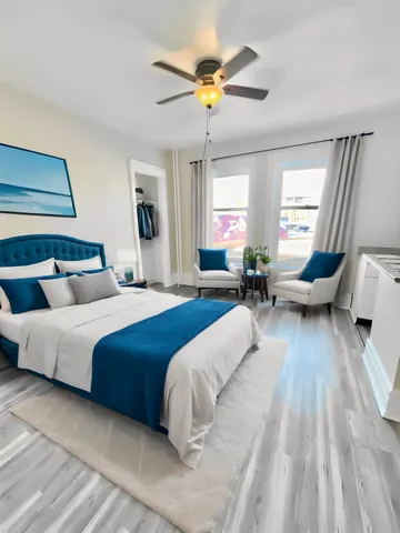 Elegant bedroom with a modern blue theme, featuring a cozy double bed, plush seating area, and abundant natural light from large windows.