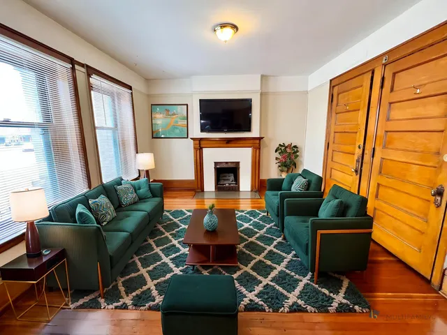 Inviting living room with elegant green sofas, cozy fireplace, and chic wooden accents, perfect for relaxation and entertainment.