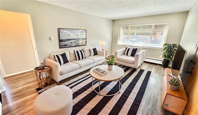 Bright living room featuring modern white sofas, striped rug, and large window with natural light.