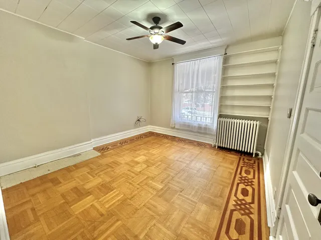 Charming room with elegant parquet flooring, decorative border, ceiling fan, and natural light streaming through a large window.