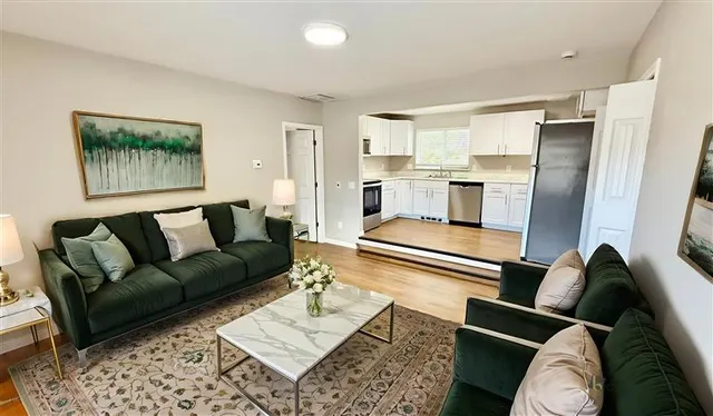 Inviting living room with elegant dark green sofas, chic coffee table, and open access to a modern, well-equipped kitchen.
