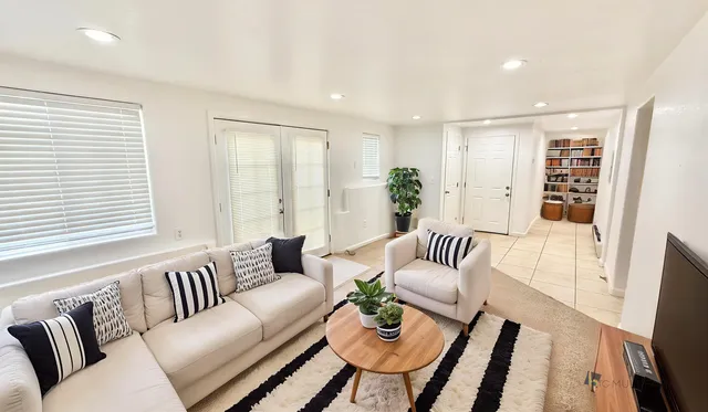 Bright and inviting living room with cozy white sofas, stylish striped cushions, and a chic wooden coffee table adorned with plants, leading to a tiled entryway with built-in shelves.