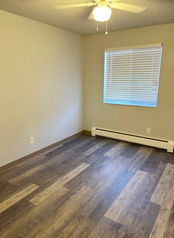 Bright and inviting room with modern wood flooring, large window, and ceiling fan creating a cozy ambiance.