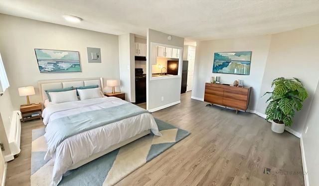 Bright and airy bedroom with modern decor, large windows, and an open layout leading to a cozy kitchen and living space.