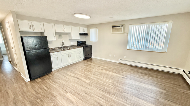 Bright open-concept kitchen and living space with modern appliances, white cabinetry, and elegant wood flooring, featuring ample natural light.