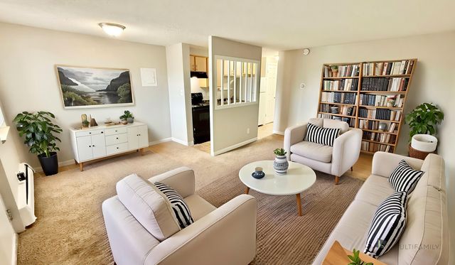 Spacious living room with modern decor, cozy seating area, and stylish bookshelf. Open access to the kitchen adds a touch of elegance.