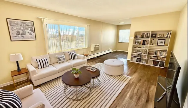 Inviting living room with plush sofas, modern coffee table, and stylish bookshelf, bathed in natural light from large windows.