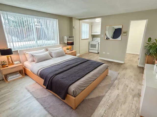 Bright and inviting bedroom with modern decor, large window letting in natural light, and a cozy view of the kitchen area.