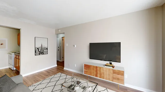 Cozy living room with modern decor, featuring a sleek TV setup, wooden floors, and open access to a quaint kitchen.