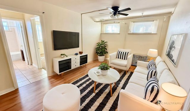 Bright, modern living room with stylish decor, featuring a comfortable white sofa, striped cushions, and lush plants. Natural light streams in through large windows.