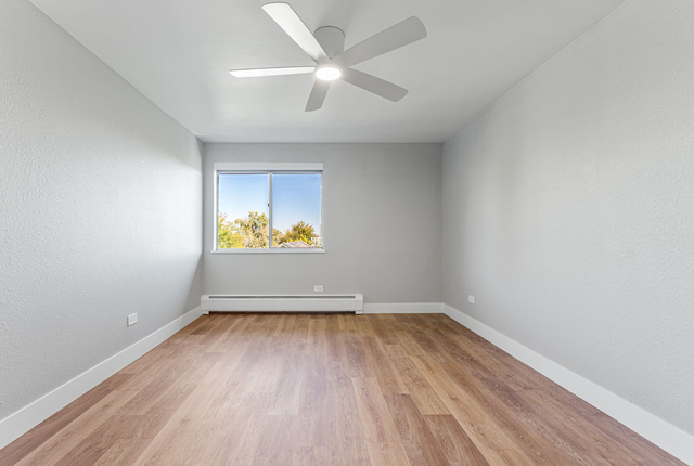 Bright, spacious bedroom with modern ceiling fan, large window offering natural light, and elegant wood flooring.
