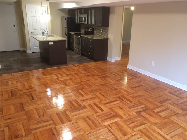 Charming open-concept kitchen and living area with elegant parquet flooring, modern appliances, and stylish dark wood cabinets.