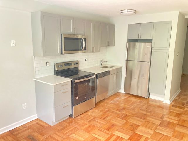 Modern kitchen with stainless steel appliances, elegant gray cabinets, and parquet hardwood flooring.