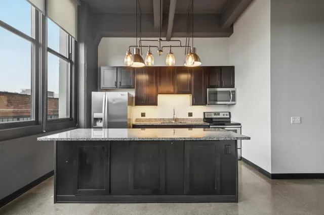 Modern kitchen with granite countertop, stylish pendant lighting, stainless steel appliances, and large windows offering ample natural light.
