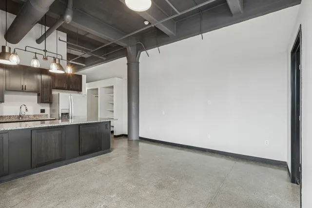 Modern industrial kitchen with dark cabinets, granite countertops, and open shelving, featuring stylish pendant lighting and sleek concrete flooring.