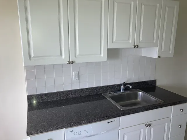Modern kitchen with sleek white cabinets, elegant tile backsplash, and a polished granite countertop with built-in sink.