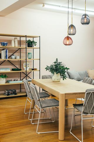 Contemporary dining space with a sleek wooden table, modern pendant lights, and stylish decor on a shelving unit.