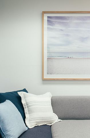 Inviting living room corner with cozy cushions and serene beach artwork in a natural wood frame.