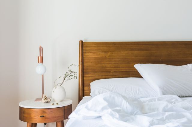 Elegant bedroom corner with a cozy wooden bed and stylish nightstand featuring a modern lamp and decorative vase.