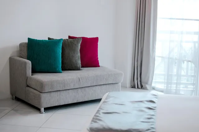 Contemporary living room with a sleek gray sofa adorned with vibrant teal and magenta cushions, bathed in natural light from large windows.