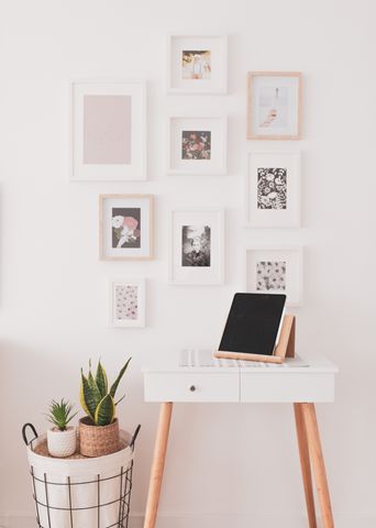 Chic modern decor featuring a stylish gallery wall, minimal desk with tablet stand, and potted plants on a wicker basket.