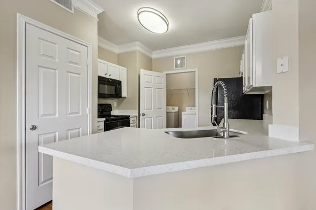 Modern kitchen with sleek white countertops, integrated sink, stainless steel appliances, and adjacent laundry room.