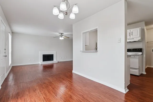 Inviting open-concept living room with wood-style floors, a cozy white brick fireplace, and a modern chandelier, adjacent to a functional kitchen.