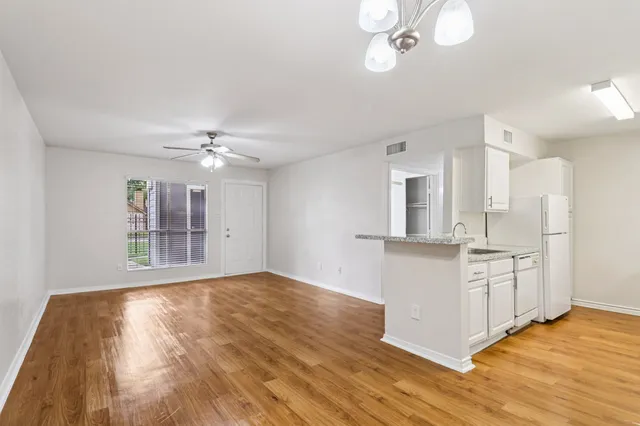 Charming open-concept living space with bright lighting, wood-style floors, and a modern kitchen featuring sleek countertops and white cabinetry.
