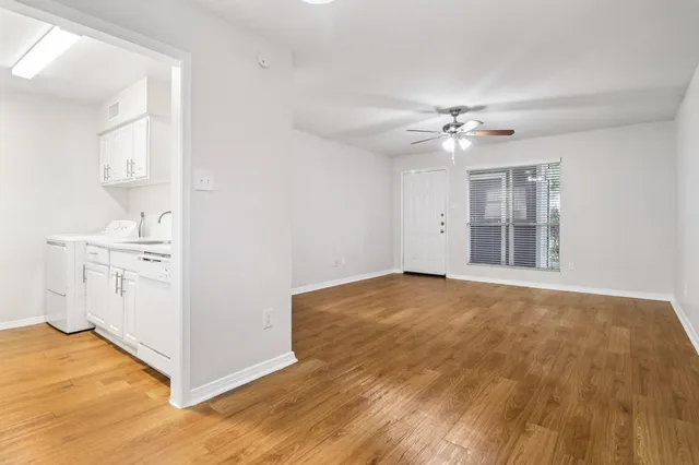 Bright living area with elegant wood-style flooring, adjacent to a modern kitchen with white cabinetry and a built-in laundry space.