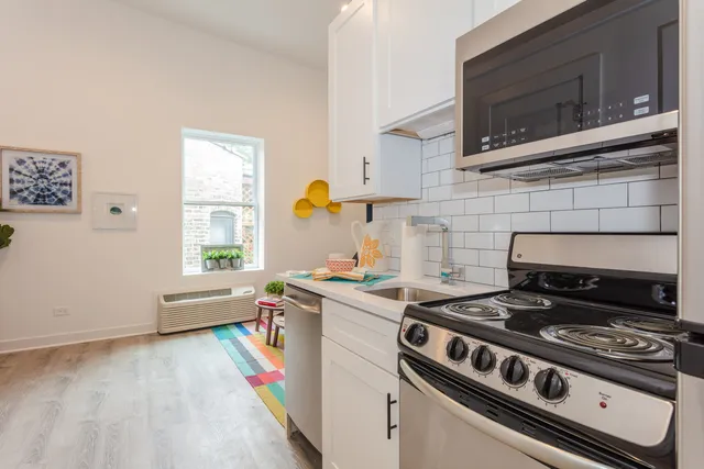 Chic modern kitchen with sleek stainless steel appliances, bright white cabinetry, and cozy window view, enhanced by a colorful accent rug.