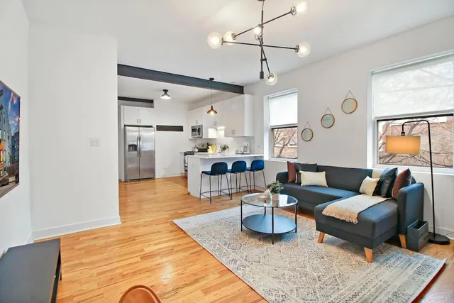 Contemporary open-concept living space featuring a stylish kitchen with bar seating, modern lighting, and a cozy living area with large windows.