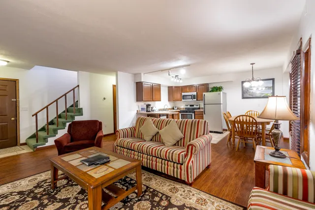 Cozy open-concept living room with striped furniture, modern kitchen with stainless steel appliances, and inviting dining area.