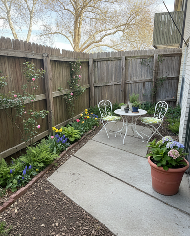 Charming garden patio featuring a cozy bistro set surrounded by colorful blooming flowers and lush greenery.