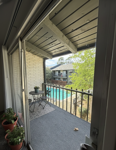 Charming apartment balcony with cozy seating overlooking a refreshing pool and lush greenery.