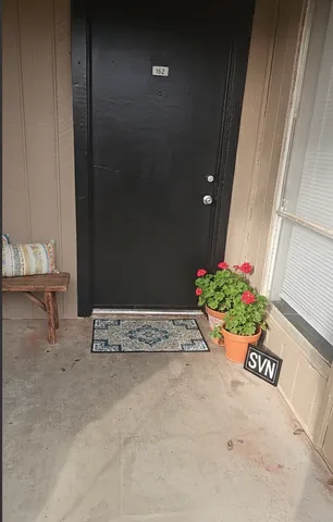 Inviting apartment entrance with a stylish black door, decorative mat, and vibrant potted red flowers.
