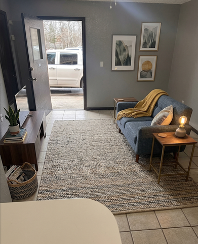 Cozy modern living room featuring a plush blue sofa, textured rug, and elegant wall art, with natural light streaming in through an open door.