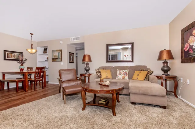 Inviting living room featuring a cozy beige sofa with decorative pillows, a stylish coffee table, and elegant wooden furniture, perfectly complemented by warm lighting and chic artwork.