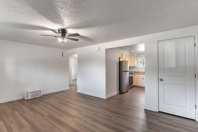 Bright and modern open-concept living area with sleek ceiling fan and hardwood floors, leading into a stylish kitchen with stainless steel appliances.