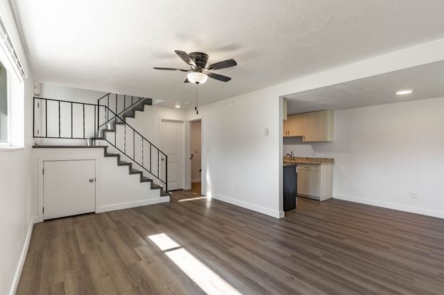 Inviting open-concept living area with modern laminate flooring, stylish ceiling fan, and adjacent kitchen. Elegant staircase leading to upper floor. Ideal for comfortable living.